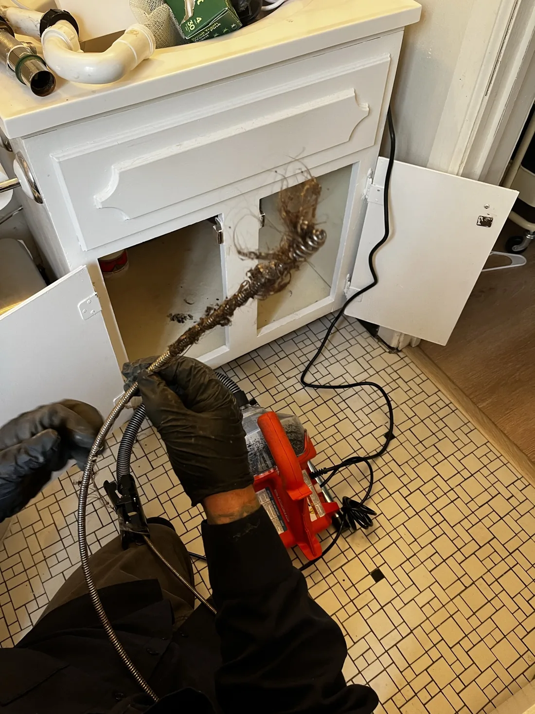 Act Now Pros technician clearing a blocked bathroom drain line with a drain cleaning machine